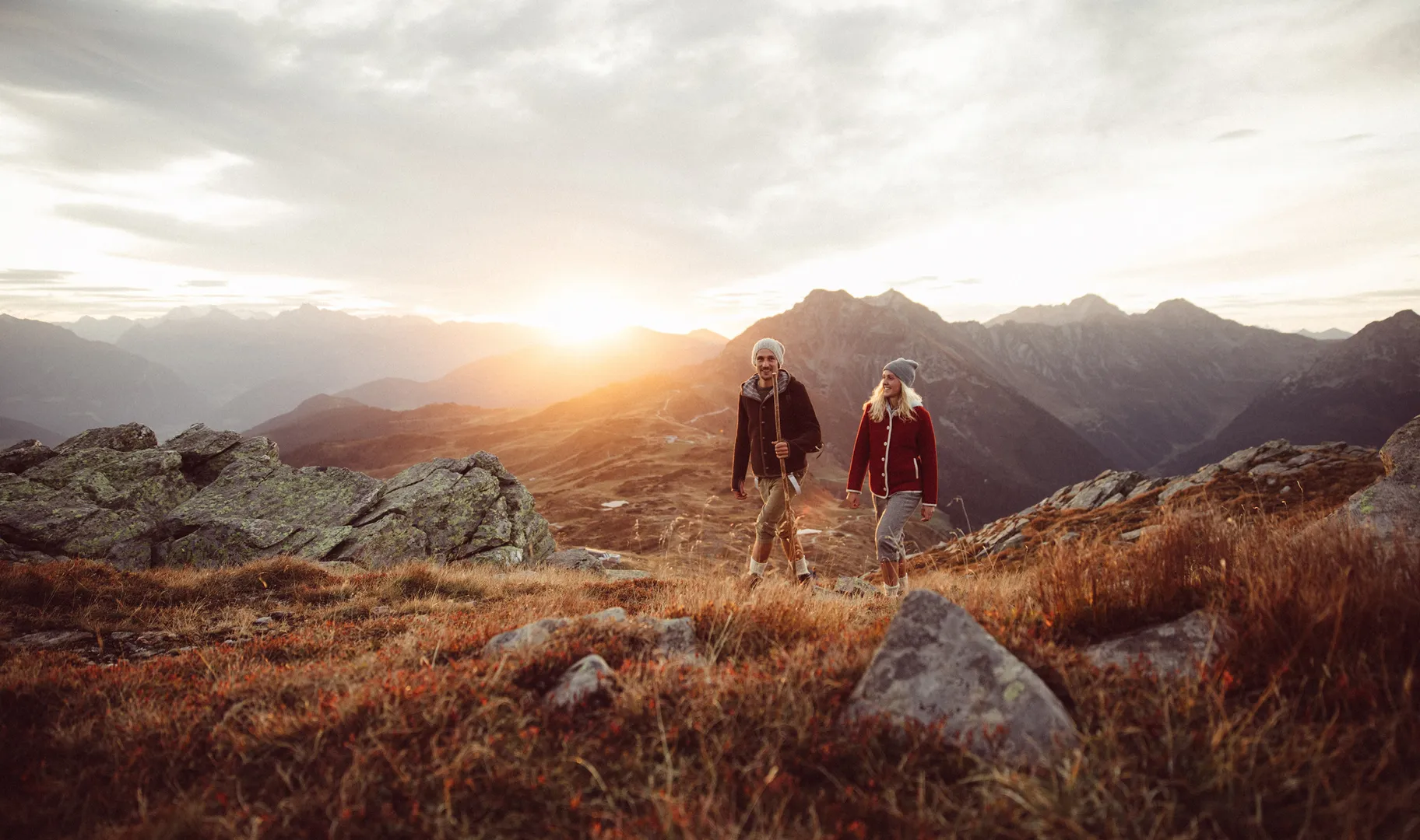 Wanderpaar mit roter und brauner Walkjacke bei Sonnenuntergang im Bergpanorama