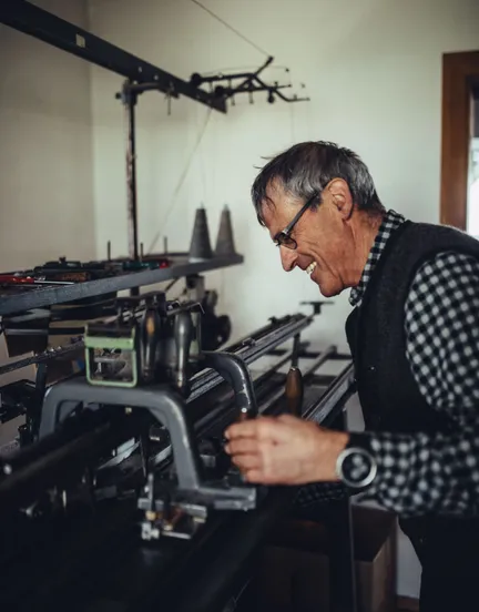 Lachender Strickmeister bedient eine alte mechanische Strickmaschine zur Herstellung von Sarner-Jacken