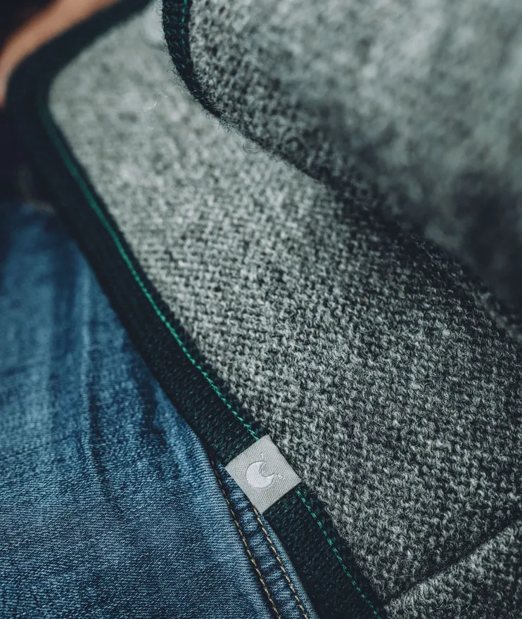 Nahaufnahme grauer Walkstoff mit grüner Einfassung und Spinnradl-Label auf Jeansstoff