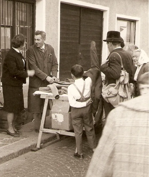 Schwarz-Weiß-Foto eines Händlers mit Wollwaren am Straßenstand mit Kunden in Tracht