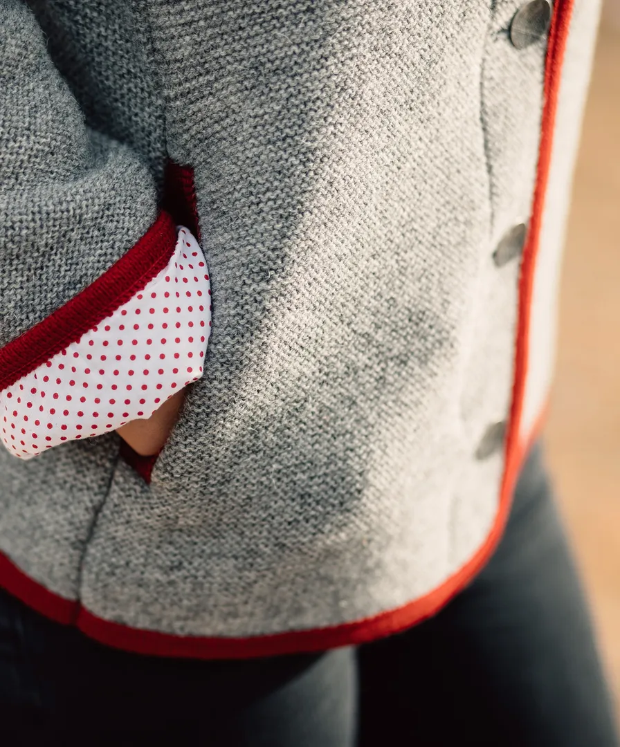 Detailaufnahme grauer Strickjanker mit roter Paspelierung und weiß-rot gepunktetem Innenfutter