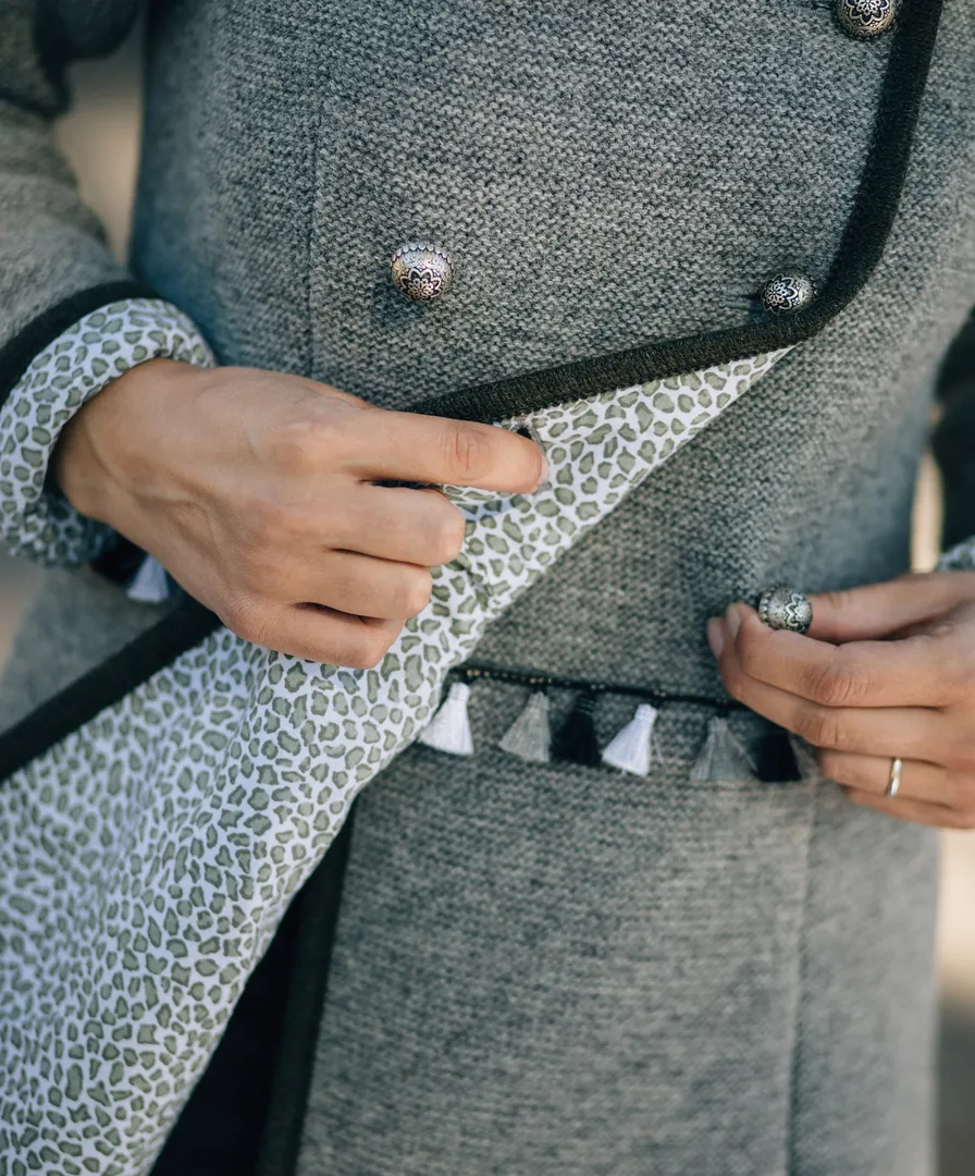 Detail eines grauen Strickjankers mit Zierknöpfen, Quasten und gemustertem Innenfutter